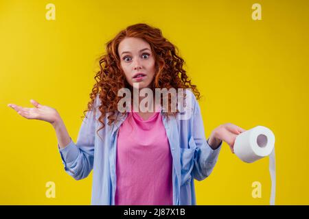 Belle femme au gingembre rouge curly tenant un rouleau de papier toilette ECO sur fond jaune Banque D'Images