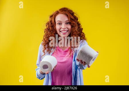 Belle curly redhead gingembre femme choisissant ECO papier toilette rouleau sur fond jaune Banque D'Images