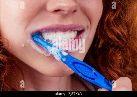 une femme au gingembre rougeâtre se brossant les dents avec de la pâte dentifrice eco sur fond jaune studio Banque D'Images