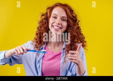 une femme au gingembre rougeâtre se brossant les dents avec de la pâte dentifrice eco sur fond jaune studio Banque D'Images