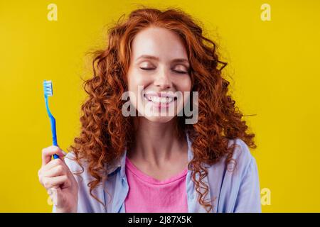 une femme au gingembre somnolent et rougeâtre se brossant les dents avec du dentifrice eco-pâte sur fond jaune studio Banque D'Images