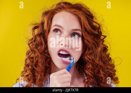 une femme au gingembre somnolent et rougeâtre se brossant les dents avec du dentifrice eco-pâte sur fond jaune studio Banque D'Images