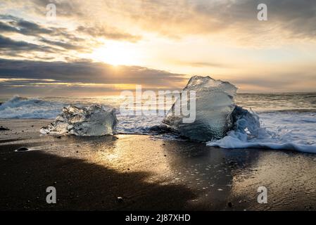 Vue à couper le souffle de blocs de glace rétroéclairés lavés sur la plage de sable noir de Diamond, Breiðamerkursandur au crépuscule, à côté de Jökulsárlón, Vatnajökul, Islande Banque D'Images
