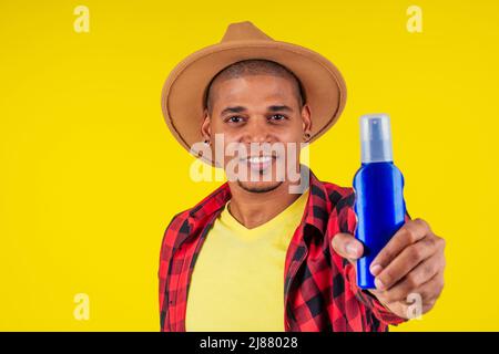 afro brésilien homme choisissant la bouteille spf dans le mur jaune studio Banque D'Images