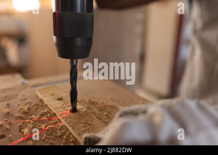 Menuisier afro-américain mature faisant du trou avec un foret sur la planche à l'atelier Banque D'Images