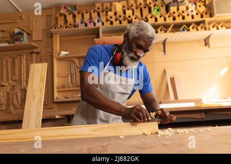 Le charpentier afro-américain mature planait de la planche tout en travaillant dans l'atelier Banque D'Images