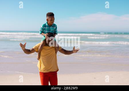 Heureux africain jeune homme américain portant son fils sur les épaules tout en se tenant contre la mer et le ciel Banque D'Images