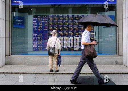 Tokyo, Japon. 13th mai 2022. Un homme tenant un parapluie marche devant un panneau électrique montrant Nikkei index une maison de courtage à Tokyo. Crédit : SOPA Images Limited/Alamy Live News Banque D'Images