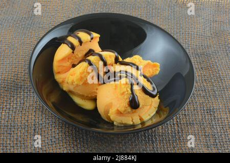 Deux boules de sorbet orange avec garniture au sirop de chocolat dans un bol noir sur toile grise Banque D'Images