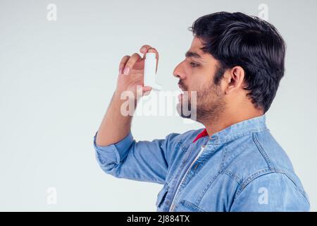Jeune indien dans une veste de jeans en denim utilisant un inhalateur d'asthme sur fond blanc de studio Banque D'Images