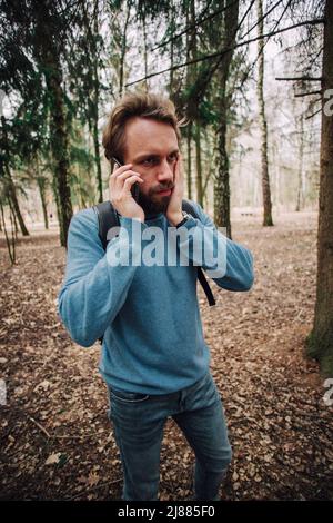 Young adult man talking on the phone debout au-dessus de mur de brique blanche a souligné avec la main sur la tête, choqué par la honte et la surprise face, en colère et frustr Banque D'Images