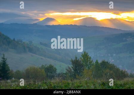 Soirée d'été dans les Carpates ukrainiens. Montagnes boisées et petits villages. Les derniers rayons du soleil se brisent à travers les nuages spectaculaires Banque D'Images