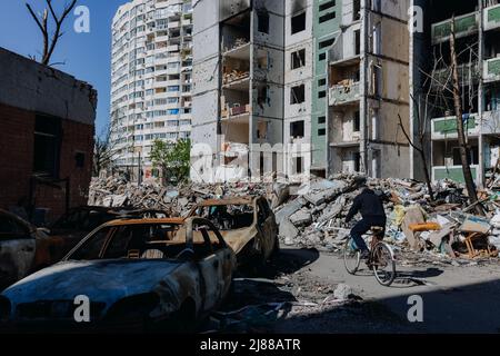 Chernihiv Ukraine 2022: Un homme fait un vélo près d'un bâtiment détruit et de voitures après une grève aérienne. Ruines pendant la guerre de la Russie contre l'Ukraine. Élevée Banque D'Images