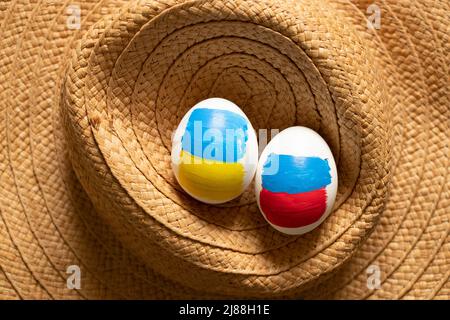 Deux oeufs de poulet, l'un avec le drapeau de la Russie, et le second avec le drapeau de l'Ukraine sur un chapeau de paille, la Russie et l'Ukraine guerre, Pâques et culture 2022 Banque D'Images