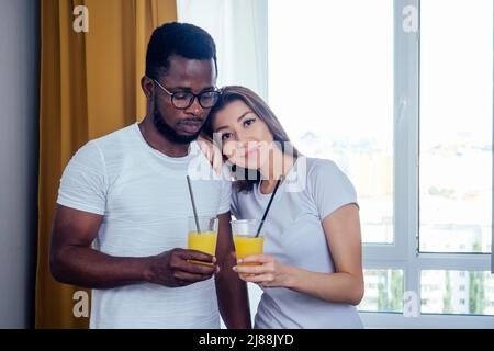 couple international dans l'amour tenant dans les mains verres avec le jus d'orange.afro homme utiliser la vaisselle jetable, mais la femme européenne utilisant des tubes en acier éco Banque D'Images