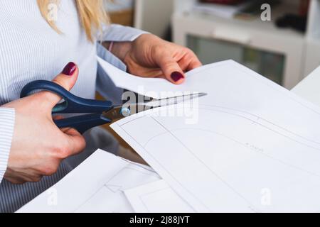 La couturière coupe des motifs de paper pour la robe avec des ciseaux. Développement de conception et création de vêtements Banque D'Images