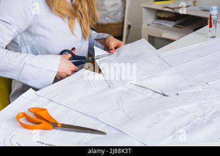 La couturière coupe des motifs de paper pour la robe avec des ciseaux. Développement de conception et création de vêtements Banque D'Images