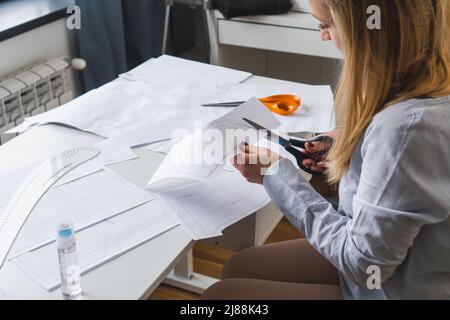 La couturière coupe des motifs de paper pour la robe avec des ciseaux. Développement de conception et création de vêtements Banque D'Images