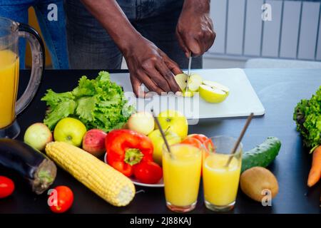 gros plan de hamds afro mâles coupant pomme, aubergine et kivi Banque D'Images