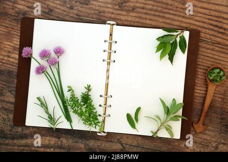 Livre de recettes avec des pages ouvertes et des herbes fraîches de jardin de cuisine utilisé dans l'assaisonnement alimentaire et la médecine de plantes sur fond de bois rustique. Pose à plat. Banque D'Images