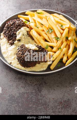 Le steak au poivre ou au poivre est un plat français qui se compose d'un filet mignon, recouvert de grains de poivre grossièrement craquelés, servi avec des frites cl Banque D'Images