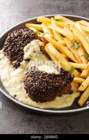 Steak maison au poivre accompagné de sauce au poivre servi avec des frites dans une assiette sur la table. Verticale Banque D'Images