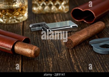 Deux cigares cubains et un briquet dans un étui en cuir sur une table brune ancienne. Verre de whisky sur un arrière-plan flou. Banque D'Images