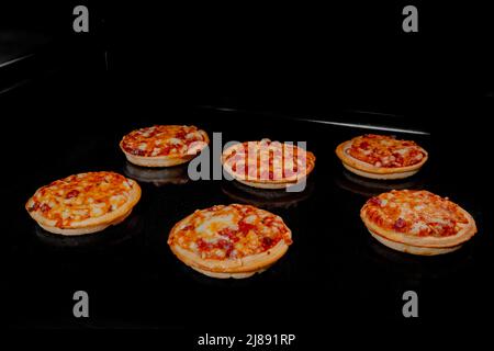 Six mini pizzas maison brûlées sur plateau dans four électrique, fond noir Banque D'Images