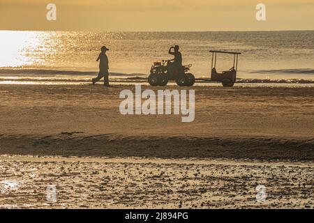 Silhoutte d'un homme à bord d'un véhicule tout-terrain et d'une dame qui marche contre le lever du soleil tôt le matin à la plage de Pantai Beserah près de Kuantan à Pahang, en Malaisie. Banque D'Images