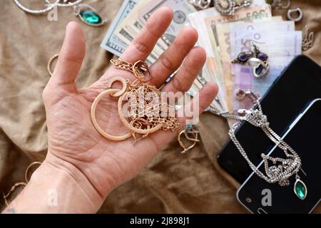 Maraudeurs main avec un tas de bijoux volés, de l'argent et des smartphones sur tissu militaire uniforme. Pillage par des soldats russes dans le citi ukrainien Banque D'Images