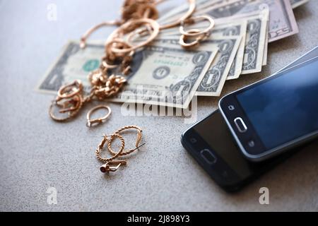 Beaucoup de bagues, boucles d'oreilles et colliers de bijoux d'or chers avec beaucoup de dollars US factures près de smartphones. Concept de la boutique de prêt-à-pattes Banque D'Images