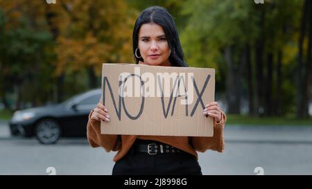 Jeune femme hispanique sérieuse militante debout à l'extérieur manifestant la bannière avec l'inscription no vax montre le signe de carton de manifestant contre Banque D'Images