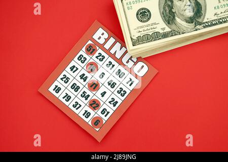 Tableau de bingo rouge ou carte à jouer pour gagner des jetons et une pile de billets en dollars. Carte de bingo classique américaine ou canadienne de cinq à cinq sur fond rouge vif Banque D'Images