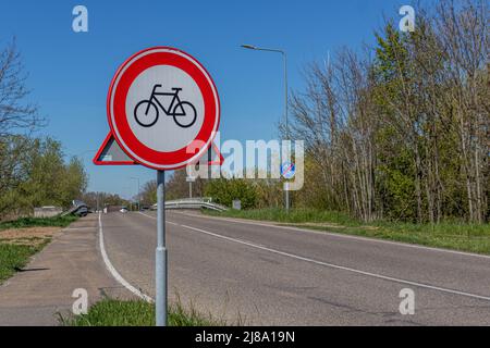 Signalisation routière indiquant: Les bicyclettes sont interdites sur une route de campagne, une plaque ronde rouge, blanche et noire, des ponts et des voitures de passage, ciel bleu à l'arrière Banque D'Images