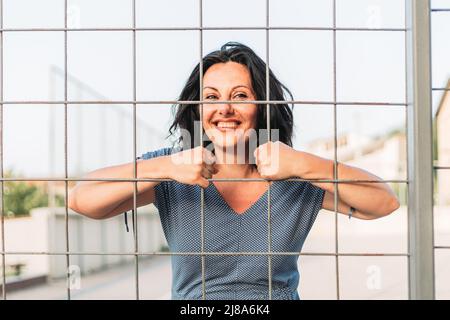 Âge moyen confiant, femme brune debout et souriante. Regarder à travers le fil Banque D'Images