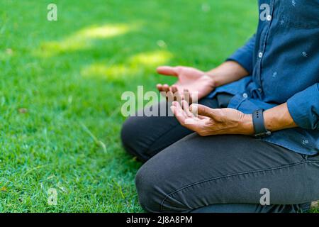 le jeune homme méditant se concentre sur les mains avec les paumes orientées vers le haut, assis sur ses genoux sur l'herbe Banque D'Images