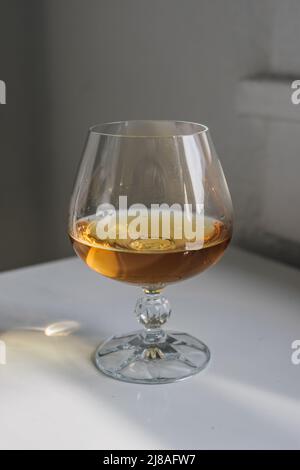 un snifter au brandy sur une table réfléchissante blanche avec un fond blanc près de la fenêtre Banque D'Images