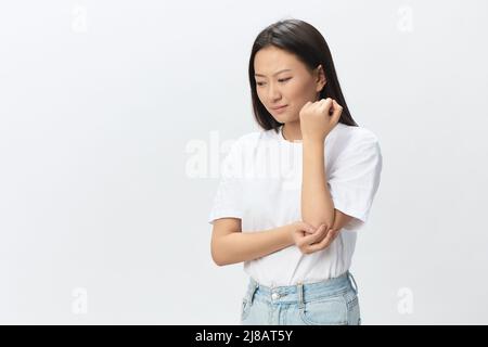 La souffrance tourmentée couvrait une belle jeune femme asiatique souffrant tenant un coude douloureux posant isolé sur fond blanc. Blessures mauvaise santé maladie Banque D'Images