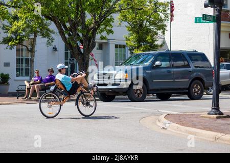 Une femme à vélo couché dans une rue animée en été. Il y a des voitures et des gens à l'arrière-plan de cette petite ville. Banque D'Images