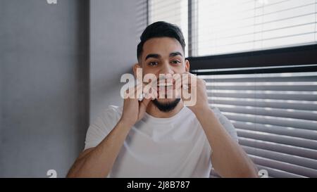 Portrait millénaire beau garçon indien arabe barbu en chemise blanche se brossant les dents en utilisant la soie dentaire matin hygiène rituel nettoyage oral toothy Banque D'Images