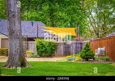 Soleil jaune voiles ombre zone de fête derrière la clôture privée de la maison paysagée entourée d'arbres verdoyants Banque D'Images