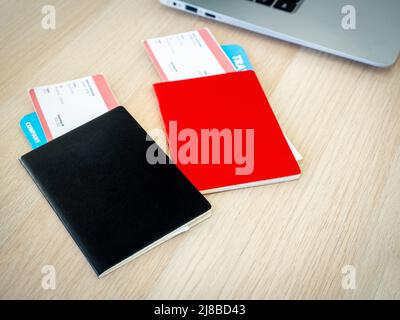 Noir et rouge, couleur différente de deux passeports avec couverture vierge avec deux billets d'avion près de l'ordinateur portable sur le bureau avec lumière du soleil. Billet en ligne Banque D'Images