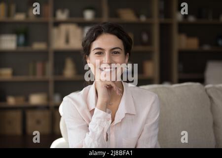 Une femme sourit en regardant l'appareil photo se détendre sur le canapé à la maison Banque D'Images