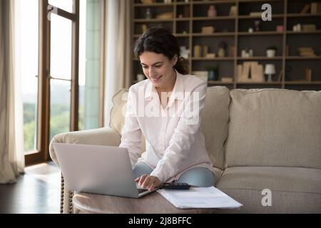 Une jeune femme s'assoit sur un canapé pour travailler ou étudier sur un ordinateur portable Banque D'Images