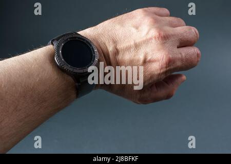 Montre intelligente avec écran noir sur la main d'un homme, gros plan sur fond gris. Banque D'Images