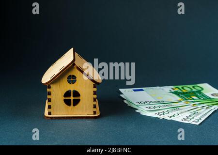 Une centaine de billets en euros devant une maison en bois sur fond gris, en gros plan. Banque D'Images