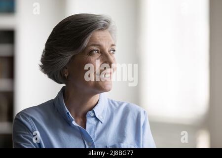Bonne femme de 60s ans regardant par la fenêtre avec espoir Banque D'Images