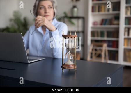 Femme d'affaires senior travaillant à un ordinateur portable par sablier sur une table Banque D'Images