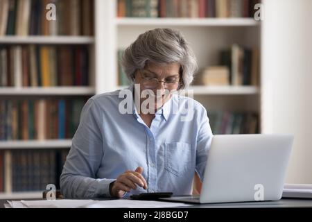 Bonne femme propriétaire senior dans des lunettes en utilisant la calculatrice Banque D'Images