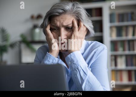 Une femme âgée frustrée se touchant la tête et regardant l'écran d'un ordinateur portable Banque D'Images